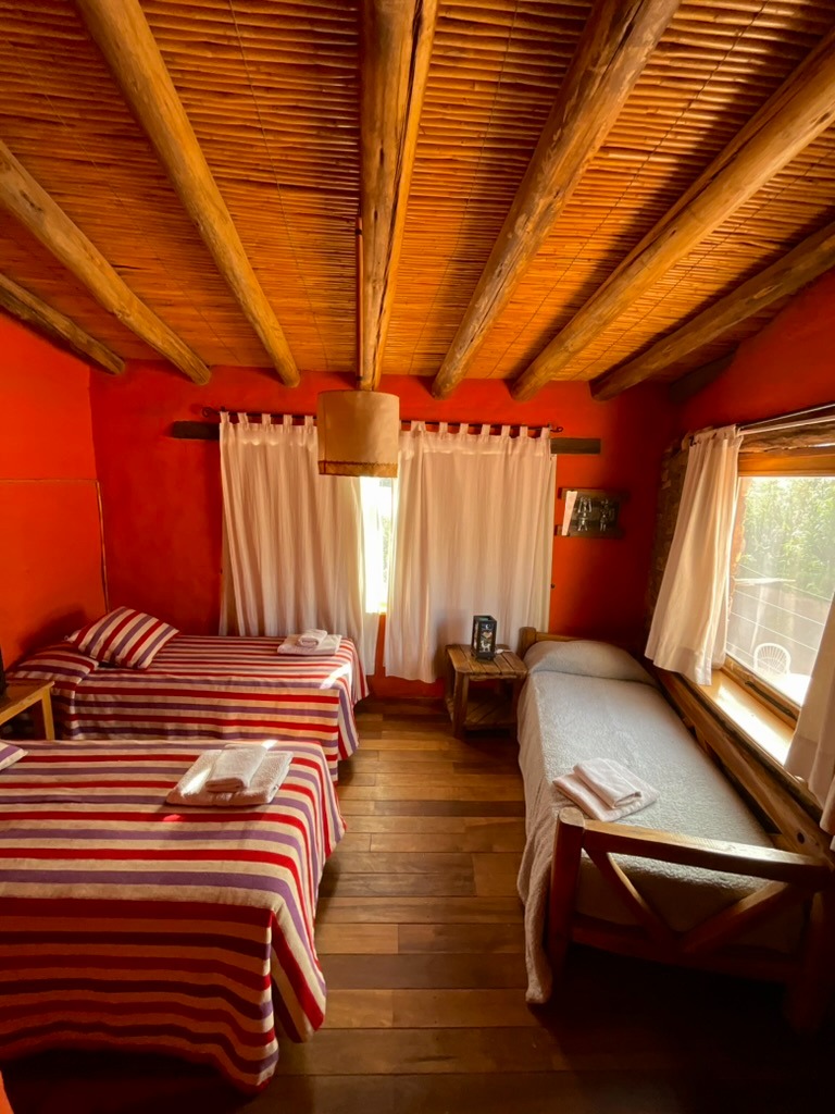 Habitación triple con paredes ocre y cubrecamas de telar andino